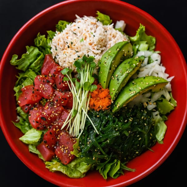 A vibrant poke bowl with tuna, crab, avocado, seaweed, and sprouts in a red bowl.