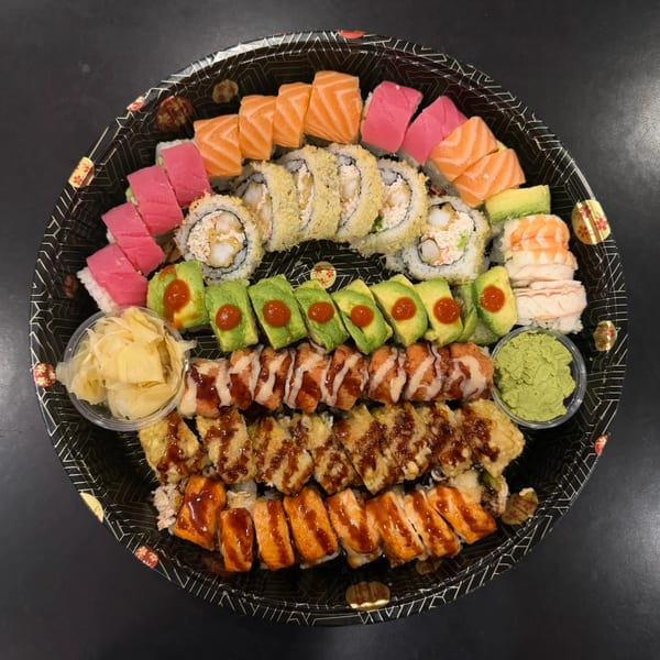A large platter of assorted sushi rolls, including salmon, tuna, avocado, and fried options, with ginger and wasabi.